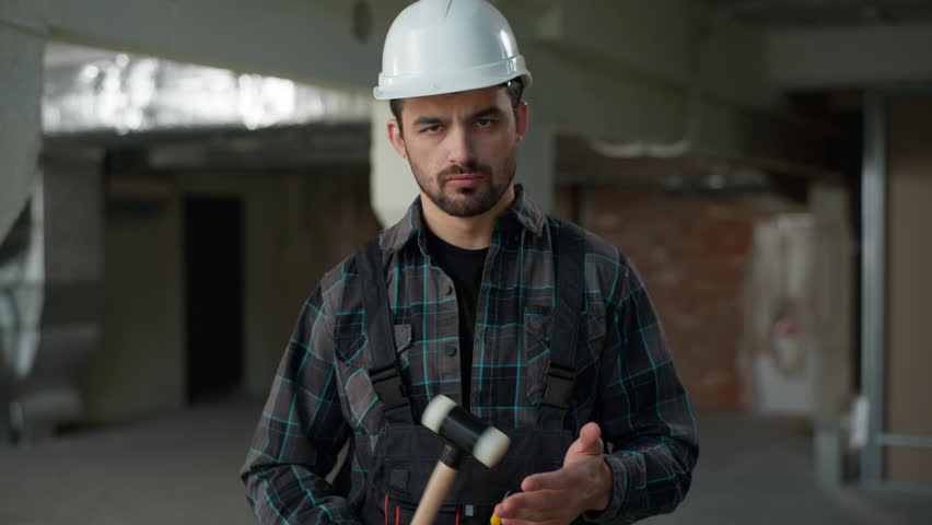 Portrait man builder repairman engineer angry guy hitting hammer on construction site building renovation annoyed industrial architect in uniform foreman handyman male rage looking at camera anger
