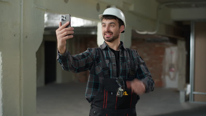Construction engineer man builder Caucasian guy male talk video call mobile phone conference chat on building site handyman foreman architect talking smartphone friendly smiling apartment renovation