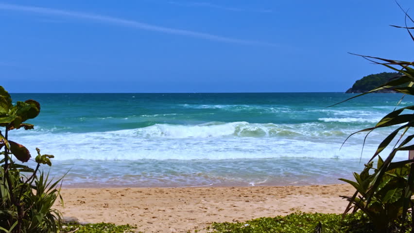A dramatic view of powerful ocean waves crashing onto a sandy beach under a cloudy, stormy sky. The scene captures the raw energy of nature and the dynamic motion of the sea.
