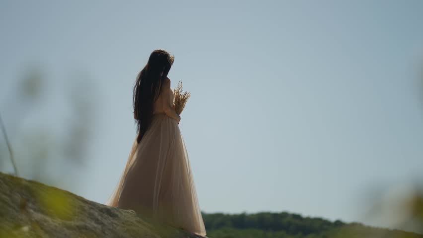 A woman in a long dress stands on top of a hill. The concept of female tenderness.