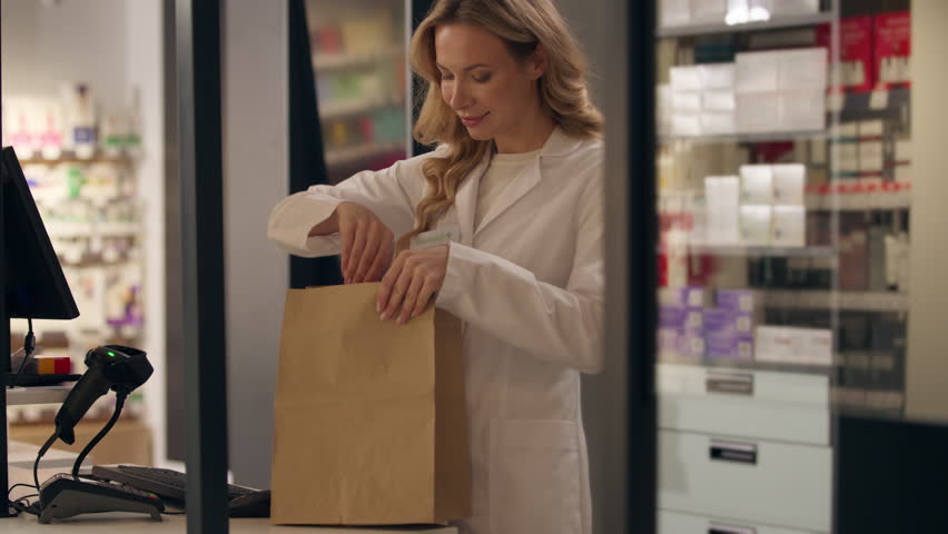 Pharmacy medication package woman doctor in coat pharmacist health care worker packing medicine order pills vitamins drugs in paper bag female Caucasian girl medical pharmacology assistant drugstore