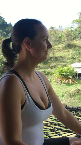 Vertical video. Woman sitting in lotus pose on bamboo terrace, surrounded by lush tropical landscape in calm morning light 