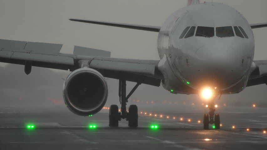Airplane is taxiing on the runway, surrounded by fog, with green lights marking the path, creating a dramatic aviation scene