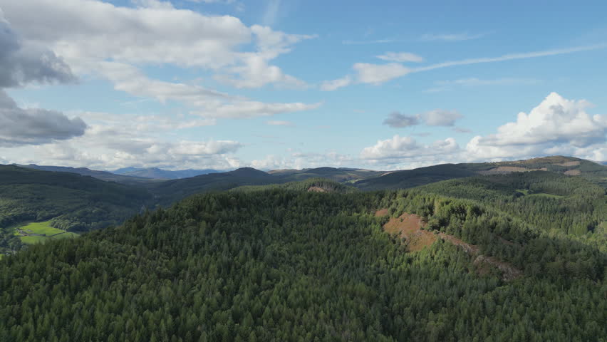 Lush green forested hills under a bright blue sky with scattered clouds.