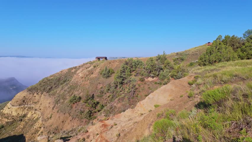 A sweeping panoramic view from the River Bend Overlook Trail at Theodore Roosevelt National Park hills partially concealed by gentle morning clouds
