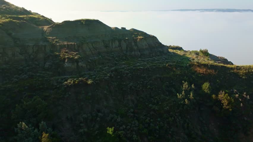 A sweeping panoramic view from the River Bend Overlook Trail at Theodore Roosevelt National Park hills partially concealed by gentle morning clouds