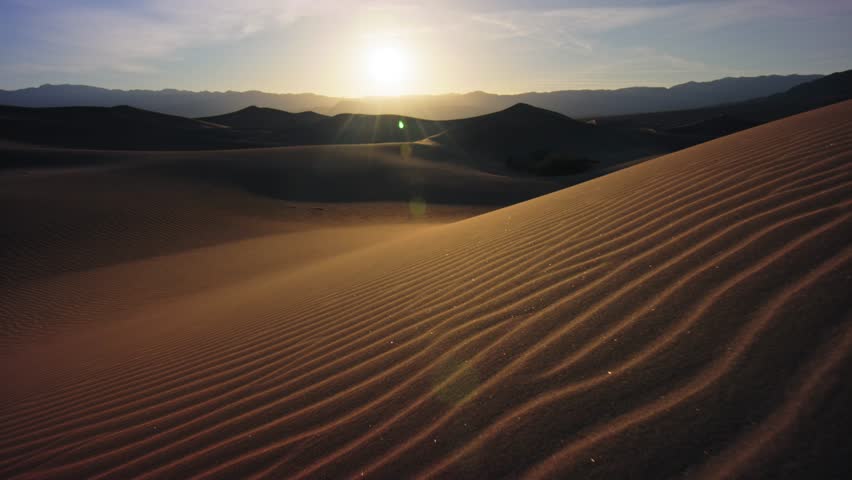 Golden hour light casting soft shadows over the sand dunes of Death Valley, highlighting the vastness and beauty of the desert landscape with rippling sand patterns