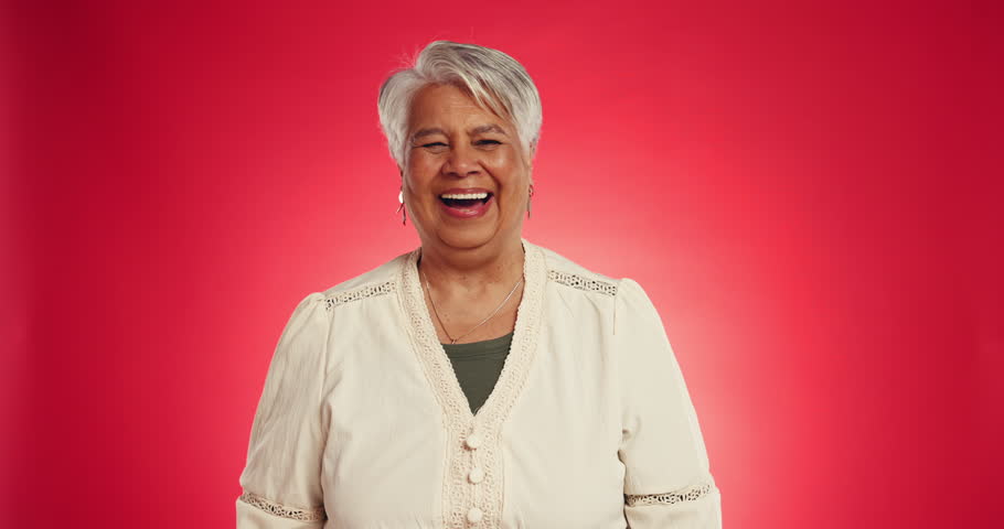 Senior, happy woman and face with laugh in studio for funny joke or humor on a red background. Portrait, elderly or female person with smile for comedy, festive spirit or positive attitude on space