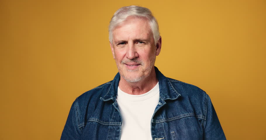Face, senior man and smile in studio for funny joke, comic story and retirement break. Portrait, elderly person and happy for laugh, positive attitude and expression of good mood on yellow background