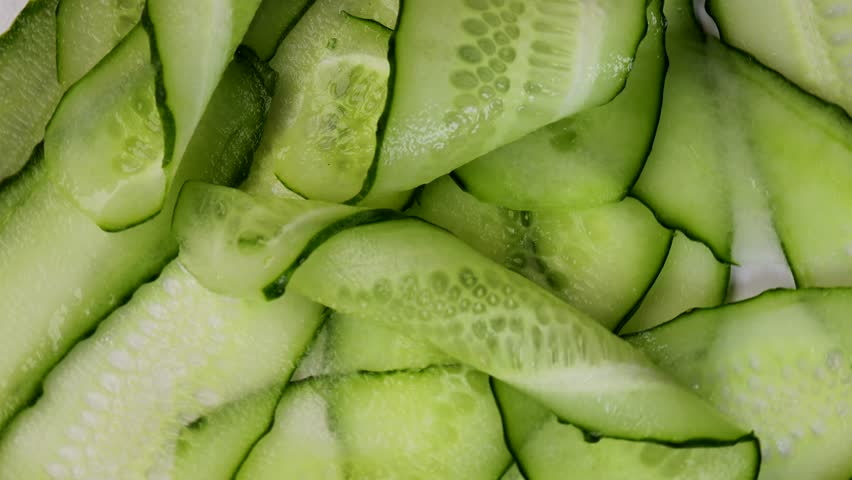 rotating thin cucumber slices in circular motion. macro video of raw green vegetable with visible texture and peel. concept of healthy eating, vegetarian cooking, food preparation
