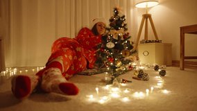 Woman in Santa Hat Lying on Floor and Smelling Cinnamon Stick near Decorated Mini Tree with Warm Lights in Cozy Room. - Powered by Shutterstock - Get 15% off with code: PIKWIZARD15