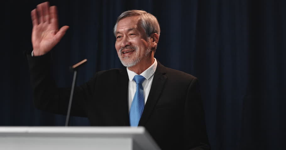 Greeting, mature man and politician on podium for election, democracy or political campaign. Speech, microphone and male speaker at conference, meeting or seminar for vote for activism at convention.