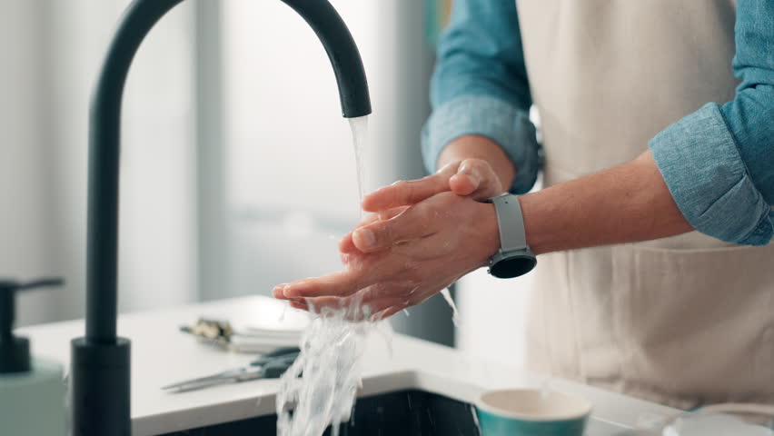 Person, water and washing hands with tap in kitchen for hygiene, disinfection or rinse in home. Closeup, chef or sink with faucet, health or safety for clean skin, bacteria or germ removal in house