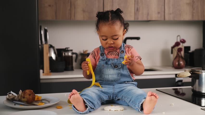 Curious toddler sitting on the kitchen counter, delightfully munching on a banana peel, showcasing a moment of innocent exploration