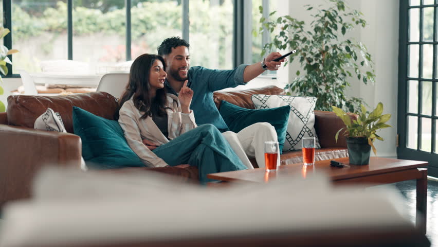 Couple, remote and watching tv with pointing on sofa for movie choice, bonding and search show. Hug, happy people and conversation in house for film subscription, weekend break and streaming service