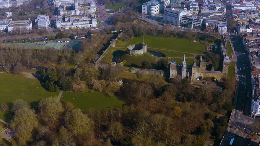 4K drone view of Cardiff Castle’s Norman motte and bailey and Gothic Revival palace in Bute Park, ringed by Cardiff city centre — an iconic Welsh capital landmark and green urban oasis.