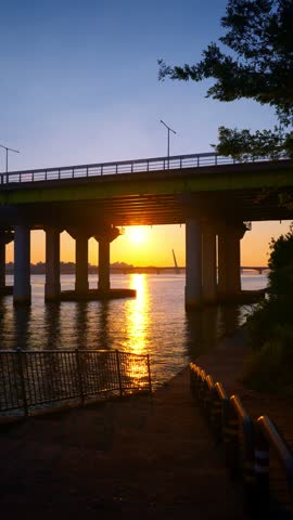 Riverfront golden sun setting over the Hangang River, framed by the silhouette of the Yanghwa Bridge in Seoul, South Korea - vertical