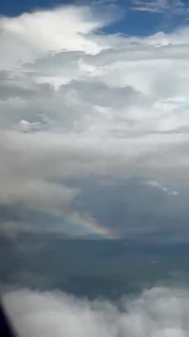 a rainbow that can be seen between rows of white clouds after rain