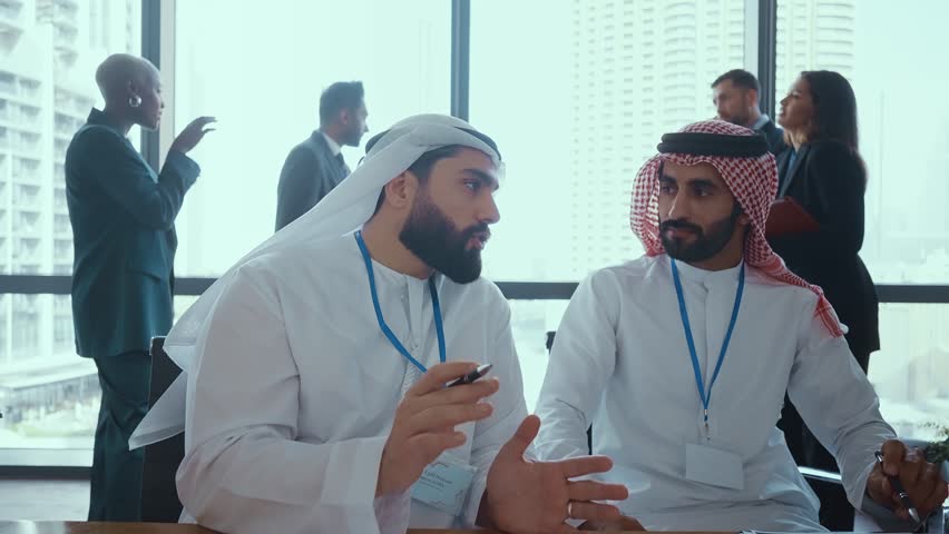 Emirati businessmen in kandura discussing in a modern office in dubai with a businesswoman in abaya, while other colleagues are working in the background