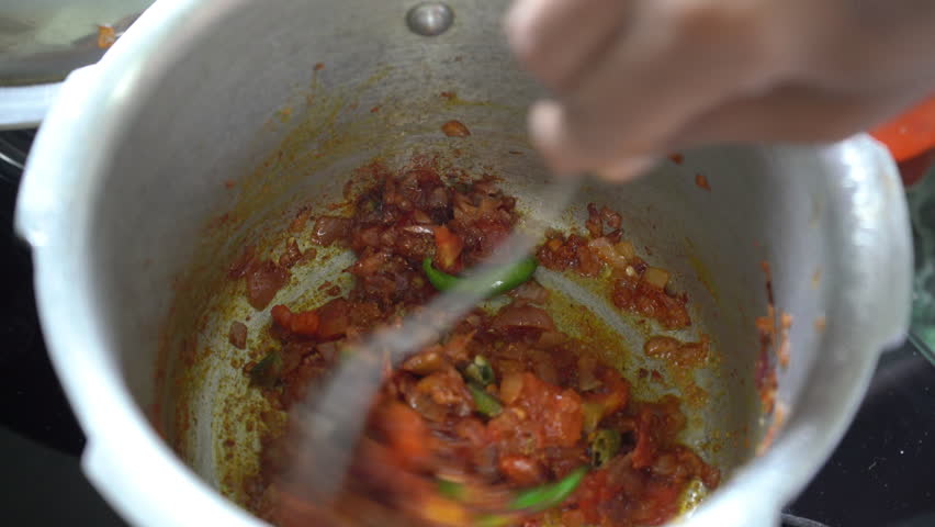 Close up view of a hand stirring traditional Indian food in a metal container