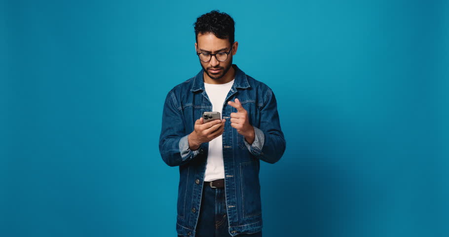 Man, phone and doubt in studio with scam, phishing and reading post on blue background. Person, smartphone and shocked with fake news, error and confused on social media with spam on mockup space