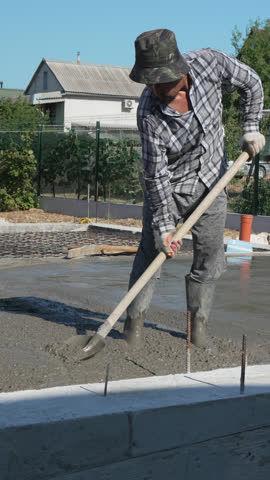 Concrete worker construction leveling foundation outdoors during daytime. Vertical video