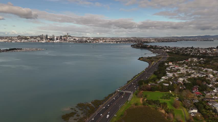 A dynamic 4K 60fps drone reveal, flying backward over motorway traffic near Shoal Bay to showcase Auckland