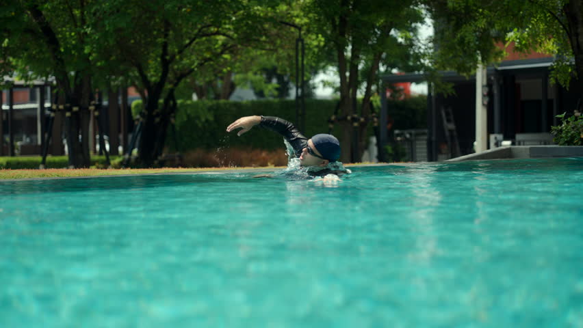 Relax moment of man in rash guard and swim cap swims laps in a clear blue pool, demonstrating an active and healthy lifestyle. The image captures motion and refreshment.