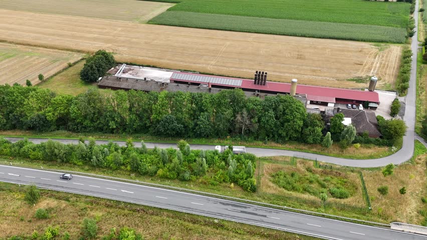 Traditional American barn in red color in rural area. Aerial lateral wide shot. Traffic on road. Sunny day in summer. Growing wheat, soy and corns on field. Peaceful neighborhood in Dakota.
