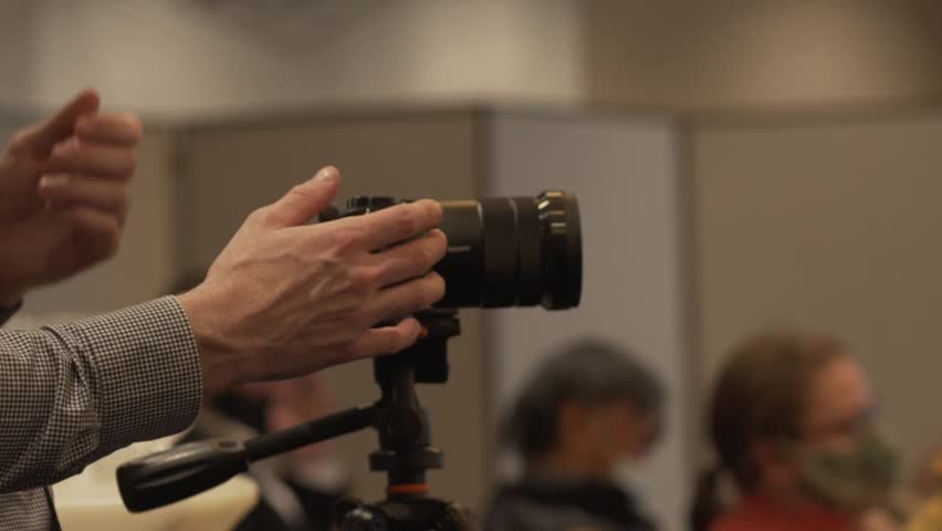 A person wearing a long sleeve shirt operates a DSLR camera. 