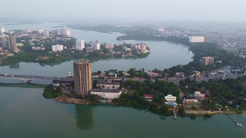This wide aerial shot captures Freetown, Sierra Leone, featuring modern high-rise buildings, a bridge bustling with traffic, lush green vegetation, and waterways blending urban and natural elements, s