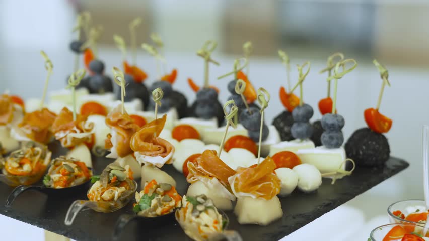 Exquisite canapes on wooden skewers with ham, cheese, grapes and cherry tomatoes. Elegant buffet appetizers for banquets and festive events catering
