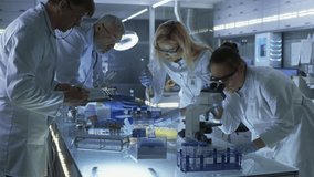 A Group of Medical Scientists in Lab Coats Work at a Laboratory. They Use Pipettes, Microscopes, and Test Tubes to Handle Samples. Laboratory Equipment, Glassware, and Computers - Powered by Shutterstock - Get 15% off with code: PIKWIZARD15