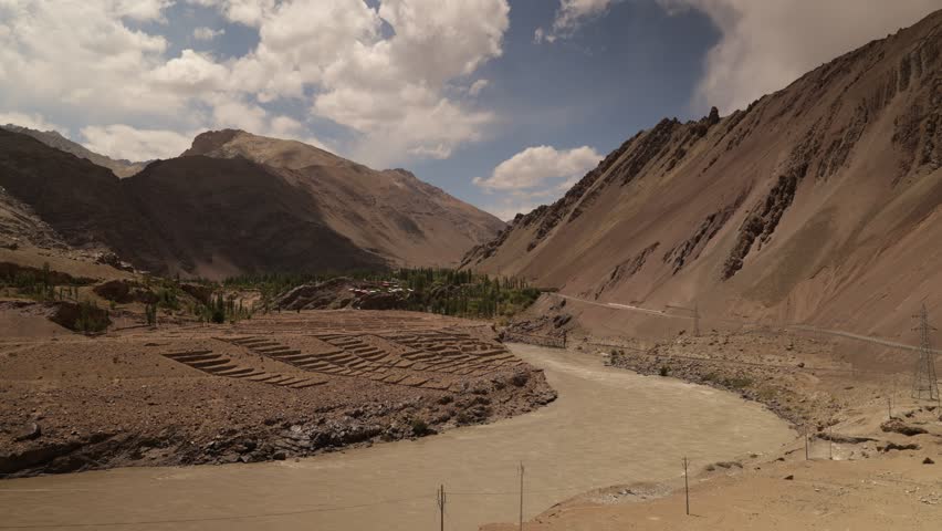 Glacial wash flowing through valley with sweeping clouds making shadow and light patterns over the rocky landscape, Ladakh region India.