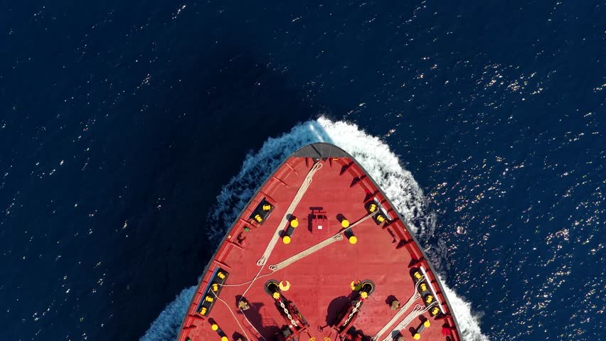 Aerial overhead view at a bow of a tanker cargo ship traveling in full speed over blue ocean