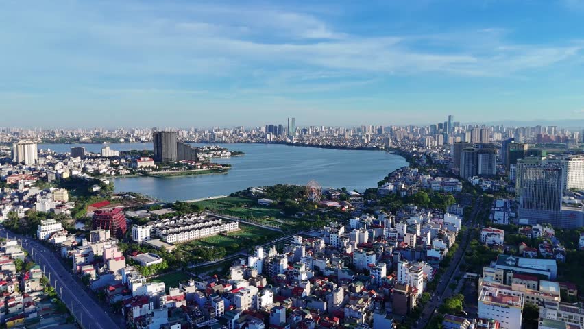 An aerial view of West Lake in Hanoi, Vietnam, with Lotte Center rising on the left and urban buildings surrounding the freshwater landmark