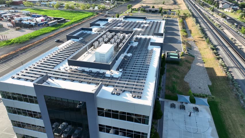 Solar panels on an office building near a golf course, railroad, and suburban neighborhood for clean energy - aerial parallax