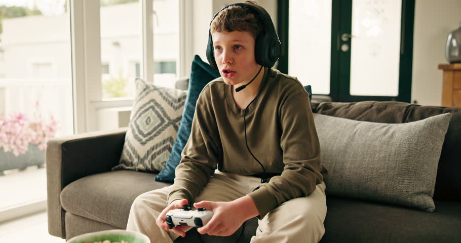Home, video game and boy on sofa, talking and entertainment with snack, console and hobby. Apartment, kid and child on couch, headset and gamer with controller, conversation and relax with tech