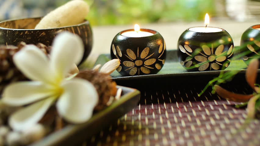 Close‑up of decorative candle holders with floral carvings and lit candles, surrounded by spa elements including plumeria flower, natural textures, and warm relaxing ambiance - Powered by Shutterstock - Get 15% off with code: PIKWIZARD15