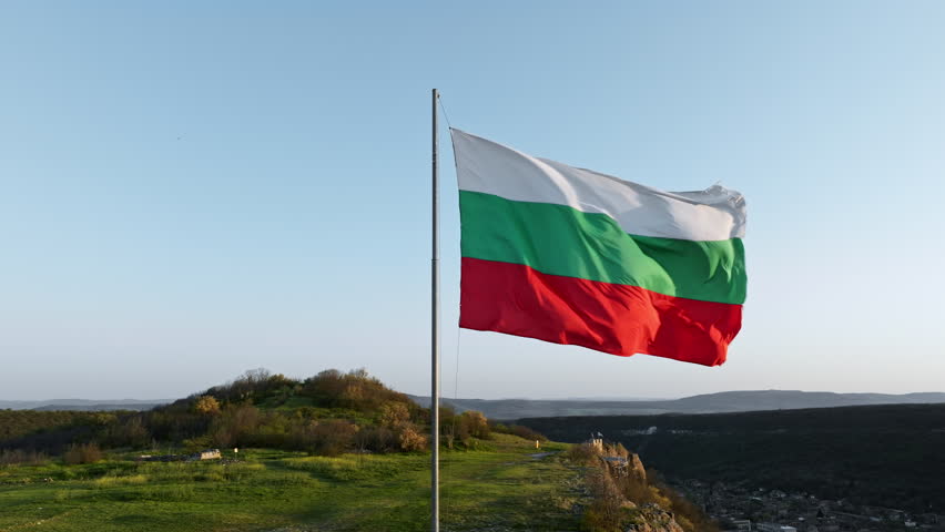 Bulgaria flag waving above Ovech Fortress, ancient stone towers and countryside in background, drone view of Balkan historic monument in summer travel season