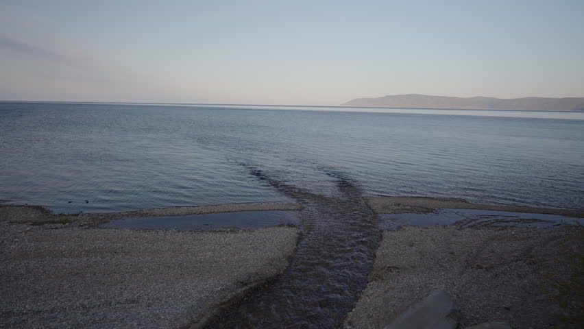 Small stream flowing gently into a calm lake at dusk, with majestic mountains rising in the background, creating a serene and tranquil atmosphere perfect for relaxation