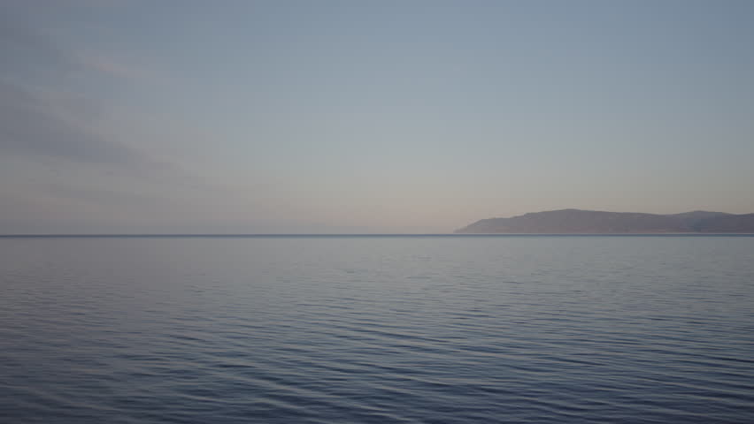 Soft pastel hues washing over glassy lake surface, mirroring dawn radiance while distant shoreline fades into misty peaceful horizon, no people, nobody. Concept of calmness, silence, unity with nature