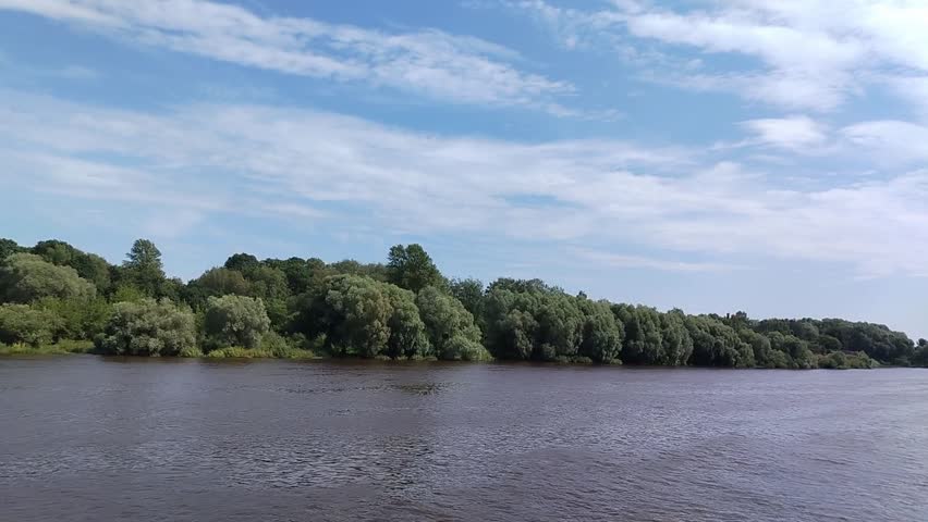 River landscape in summer, a large river, many plants on the bank, green trees and bushes.