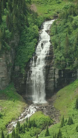 A vertical view of Reynolds Creek Falls cascading through alpine forest in Glacier National Park, Montana, surrounded by rugged mountain scenery