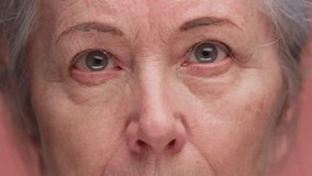 Close-up of elderly woman tired eyes on pink background - Powered by Shutterstock - Get 15% off with code: PIKWIZARD15