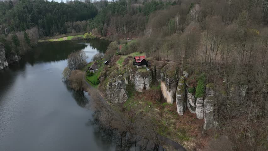 A lakeside view from above showing a house with a red roof near Rybnik Vezak, nestled in the early spring landscape of Krckovice, Czech Republic