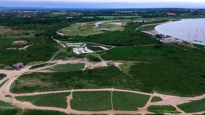 Aerial panorama: coastal landscape with rolling hills, winding roads, and serene water views.