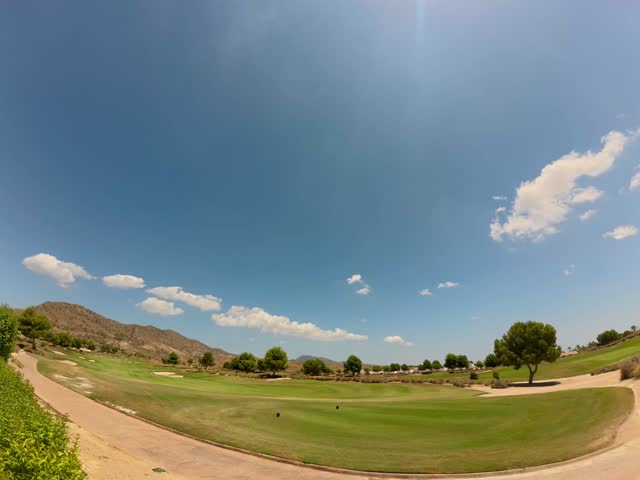 A fish-eye lens captures El Valle golf course  lush green fairways under a dramatic blue sky filled with fluffy white clouds