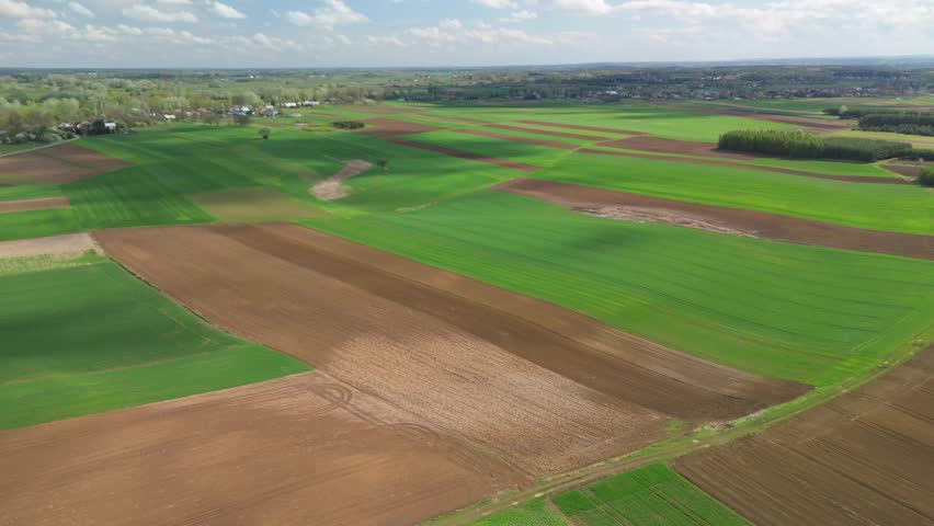 Aerial panoramic shot of expansive patchwork fields in spring, displaying colorful farmland and rural countryside.