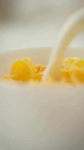 A bowl of crispy breakfast cereal is being prepared as milk is poured over it, creating a delicious meal. This moment captures the joy of starting the day with a wholesome breakfast